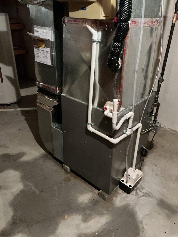 Responded to service call for condensation pump leak causing water accumulation on basement floor. Upon arrival, inspected 2-year-old furnace system and associated condensate management components. Examined white PVC condensate drain lines with red fittings, traced routing from heat exchanger through condensate pump assembly. Identified malfunction in condensate pump unit mounted at base of furnace causing improper drainage and water discharge onto concrete floor. Inspected heat exchanger coil assembly for proper condensate production and verified no blockages in drain line system. Evaluated pump operation, electrical connections, and discharge line integrity. Addressed pump issue to restore proper condensate removal function and eliminate basement floor leakage. System tested and verified operational with condensate properly draining through pump mechanism without floor discharge.