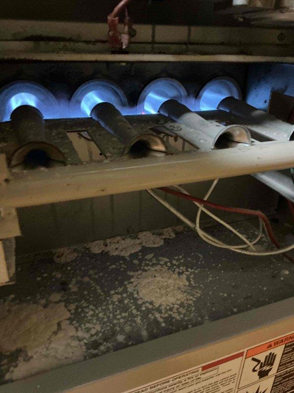 Completed comprehensive Gold AC Inspection on 2-year-old outdoor condensing unit and aging furnace system. AC unit inspected on exterior deck showed proper operation with clean condenser coils, adequate airflow through fan assembly, and secure mounting. Furnace located in basement exhibited active burner operation with visible blue flame pattern across all burners, indicating proper gas-air mixture. Heat exchanger tubes showed age-related surface oxidation consistent with older equipment but remain structurally sound. Verified all electrical connections, control wiring intact on both systems. Minor dust and debris accumulation noted in furnace base area, typical for equipment of this age. Both systems operating within normal parameters with no immediate service needs identified during routine maintenance inspection.