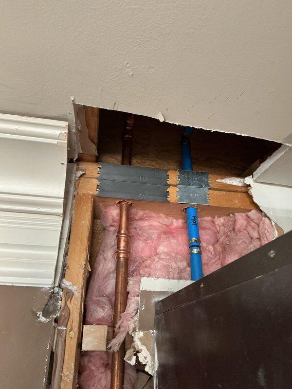 Responded to plumbing service call and accessed concealed piping system through ceiling opening to address water supply line issue. Located and inspected blue PEX and copper piping running vertically between wall studs. Removed drywall and ceiling material as necessary to gain proper access to affected plumbing components. Installed reinforcement brackets on wooden studs to secure and support piping system. Completed repair work on water supply lines and verified proper flow and pressure. Inspected basement mechanical area and removed access panel from concrete block wall to evaluate additional plumbing infrastructure and heating system ductwork for potential related issues. All affected plumbing lines tested and confirmed operational with no leaks detected.