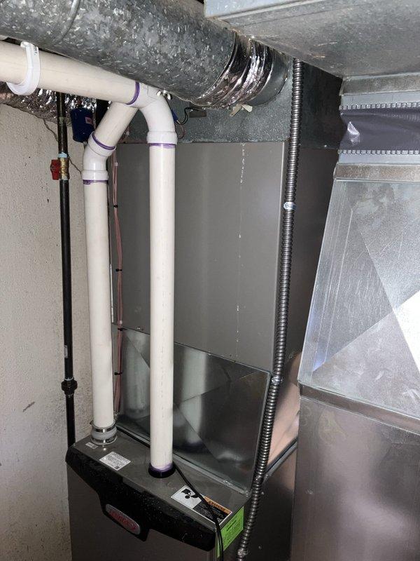 Conducted HVAC system evaluation in basement utility area for equipment replacement estimate. Assessed existing dark gray furnace unit with natural gas fuel source, vertical PVC ventilation piping, flexible ductwork, and air handler components. Documented current system configuration including electrical conduit routing, condensate drainage setup, and ductwork connections to provide comprehensive replacement recommendations for aging equipment.