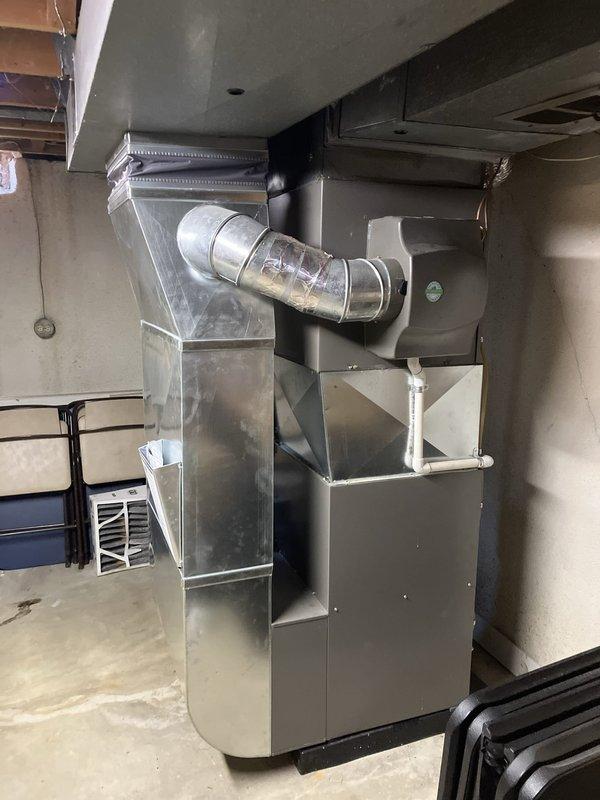Conducted HVAC system evaluation in basement utility area for equipment replacement estimate. Assessed existing dark gray furnace unit with natural gas fuel source, vertical PVC ventilation piping, flexible ductwork, and air handler components. Documented current system configuration including electrical conduit routing, condensate drainage setup, and ductwork connections to provide comprehensive replacement recommendations for aging equipment.