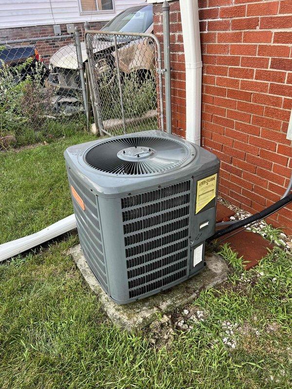 Completed comprehensive Gold AC inspection on 15-year-old residential air conditioning system with outdoor condenser unit located on exterior concrete pad and air handler in basement. Performed multi-point system evaluation including electrical diagnostics with clamp meter recording voltage at 118.6V, visual inspection of condenser unit confirming proper airflow through louvers and fan grille, and verification of refrigerant lines and condensate drainage. Unit found operating within normal parameters with no immediate service needs identified; condenser exterior shows normal weathering consistent with age, concrete pad structurally sound, and all components functioning as designed.