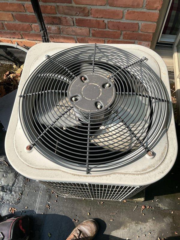 Completed comprehensive Gold AC inspection on a 3-year-old multi-unit HVAC system with air handler/coil located in basement. Performed thorough examination of outdoor condenser unit, verifying proper fan operation, inspecting wire guard assembly, checking mounting hardware integrity, and assessing overall unit condition. Confirmed system operational status, documented equipment condition with photographic evidence showing functional components with normal weathering, cleared debris from surrounding concrete pad, and verified electrical connections and refrigerant lines secure against brick exterior wall.