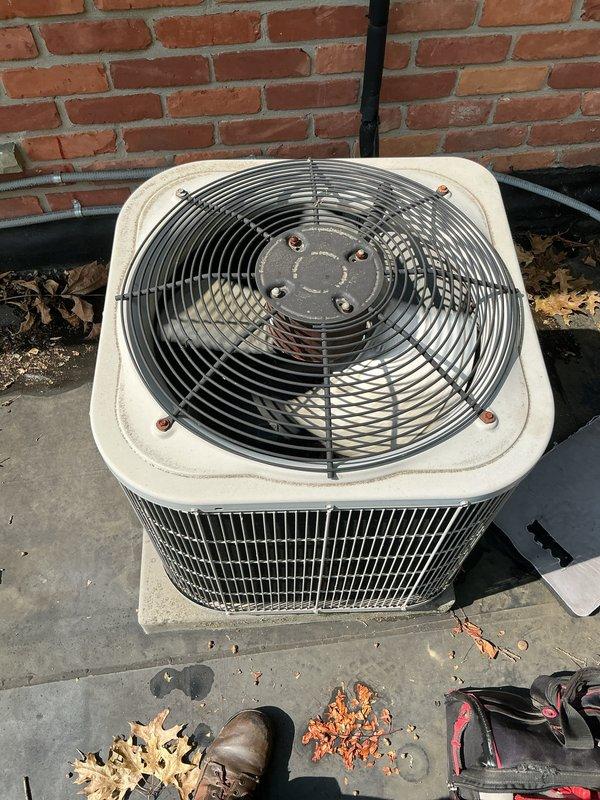 Completed comprehensive Gold AC inspection on a 3-year-old multi-unit HVAC system with air handler/coil located in basement. Performed thorough examination of outdoor condenser unit, verifying proper fan operation, inspecting wire guard assembly, checking mounting hardware integrity, and assessing overall unit condition. Confirmed system operational status, documented equipment condition with photographic evidence showing functional components with normal weathering, cleared debris from surrounding concrete pad, and verified electrical connections and refrigerant lines secure against brick exterior wall.