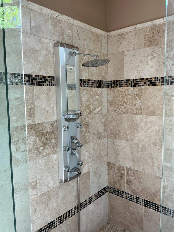 Responded to callback for persistent leak in custom shower system. Upon arrival, conducted thorough inspection of multi-function chrome shower panel with rainfall head and body spray jets. Examined all connection points, valve assemblies, and water supply lines behind decorative travertine tile work and mosaic accent bands. Traced leak source to compromised seal at shower panel mounting points. Accessed plumbing through adjacent attic space where insulation work was in progress. Tightened supply line connections, replaced faulty gaskets at panel interface, and verified all body spray jets were properly sealed. Tested system at full pressure for extended duration to confirm leak resolution. Documented conditions with photos showing shower interior and attic access area for warranty records.
