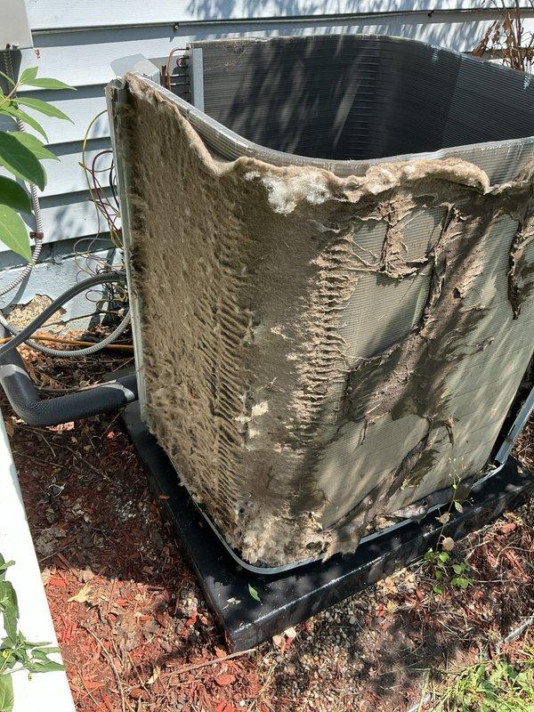 # HVAC Service Completed

Responded to no cooling complaint on 1-year-old air conditioning system. Upon arrival, located outdoor condensing unit and performed visual inspection. Found extensive damage to condenser cabinet with large sections of metal housing torn away and bent outward, exposing internal coil assembly. Noted severe deterioration with jagged edges, rust, and corrosion throughout exterior panels. Observed significant accumulation of dirt, debris, and organic material on unit surfaces and interior components.

Opened access panel to inspect internal components and discovered heavy buildup of dust and debris coating interior surfaces. Noted thick gray-brown material accumulation affecting airflow and heat transfer capability. Exterior coil fins showed dark discoloration consistent with restricted airflow and environmental contamination.

Unit condition indicated severe weathering and lack of proper maintenance. The compromised cabinet integrity and exposed coil assembly pre