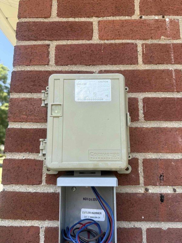 Responded to no cooling call on 13-year-old Bryant air conditioning system. Upon arrival, confirmed blower motor operating but condenser unit not running and no cooling to structure. Inspected outdoor unit and electrical connections at exterior junction box mounted on brick wall near condenser. Documented existing wiring configuration and Cutler-Hammer electrical components with installation date of November 2012. Photographed Comverge load control device and associated wiring connections for diagnostic purposes. System requires further electrical troubleshooting to determine root cause of condenser failure and restore cooling operation.