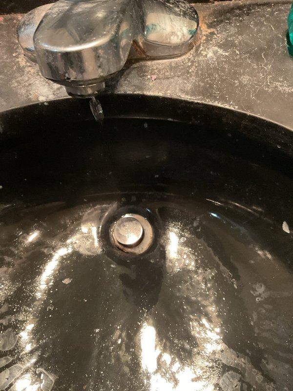 Responded to master bathroom plumbing concerns involving a slow-draining sink and leaking faucet. Upon inspection, identified issues with the chrome two-handle faucet assembly mounted on the black porcelain basin, including visible water leakage and drainage complications. Addressed the faucet leak and restored proper water flow, while also resolving the slow drain condition to return the fixture to normal operation.