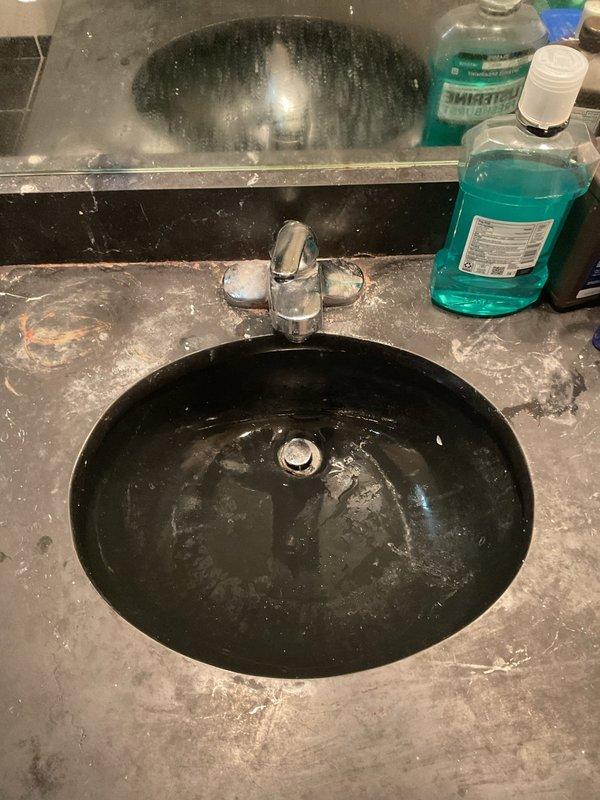 Responded to master bathroom plumbing concerns involving a slow-draining sink and leaking faucet. Upon inspection, identified issues with the chrome two-handle faucet assembly mounted on the black porcelain basin, including visible water leakage and drainage complications. Addressed the faucet leak and restored proper water flow, while also resolving the slow drain condition to return the fixture to normal operation.