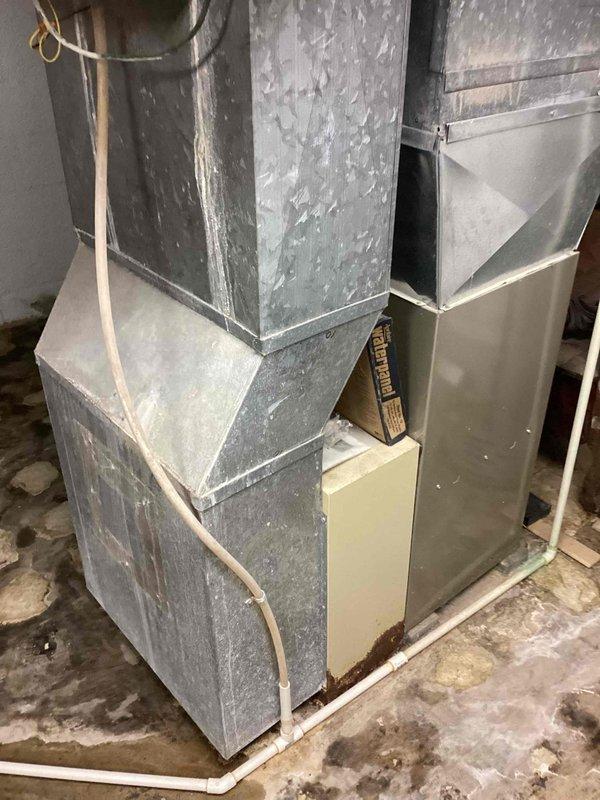 Conducted comprehensive evaluation of aging residential A/C system for replacement estimate. System is approximately 40 years old, significantly beyond its expected service life, though currently operational. Assessed existing ductwork infrastructure in basement utility area, noting galvanized metal construction with visible weathering, accumulated dust, and deterioration. Documented condition of ventilation components including curved ductwork sections showing extensive paint degradation and surface deterioration. Evaluated installation environment and accessibility for future equipment replacement, photographed existing system configuration and surrounding mechanical space to support equipment sizing and installation planning recommendations.
