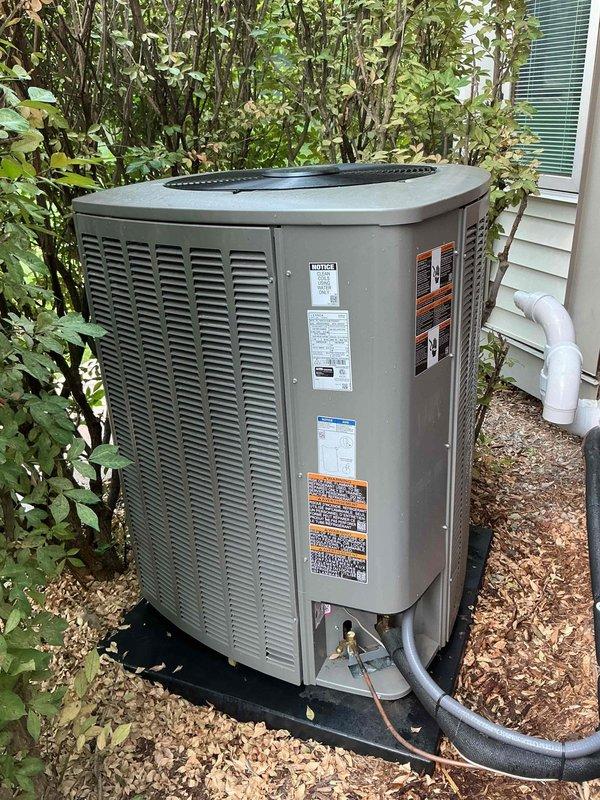 Completed comprehensive Gold AC inspection on residential air conditioning system less than one year old. Performed thorough evaluation of outdoor condensing unit including visual inspection of cabinet condition, refrigerant line connections, and proper clearances from surrounding vegetation. Verified unit operational status, checked manufacturer labels and specifications, inspected condensate drain line routing, and confirmed adequate airflow around equipment. System found to be operating normally with no immediate service concerns identified.