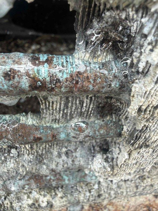 Responded to no cooling call for 20+ year old air conditioning system located in basement. Upon arrival, found unit completely inoperative with no power to system. Inspection revealed severely corroded refrigerant lines with extensive turquoise-green copper oxidation and brown rust deterioration throughout piping. Corrosion was systemic across all visible pipe sections, indicating long-term moisture exposure and environmental damage. Metal surfaces showed heavy pitting, flaking, and mineral deposits with original finish completely obscured. Given the age of equipment exceeding two decades and the extent of corrosion damage to critical components, recommended full system replacement as most cost-effective solution. Advised homeowner that attempting repairs on equipment of this age with this level of deterioration would not be economical or reliable. System has reached end of serviceable life.