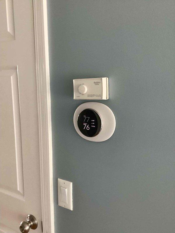 Conducted comprehensive assessment of existing HVAC system for equipment replacement estimate. Documented current thermostat installation and control system configuration, photographing wall-mounted digital thermostat displaying operational status at 77°F and associated HVAC control panel. Evaluated interior equipment location and accessibility to provide accurate replacement recommendations and system specifications.
