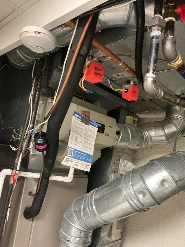 Responded to service call for water leaking from basement tube and home not cooling to thermostat setting. Performed diagnostic inspection of HVAC system and located source of water leak at evaporator coil assembly. Inspected condensate drain system, evaporator coil, refrigerant lines, and air handler components in mechanical space. Documentation photos captured of heat exchanger assembly, copper refrigerant lines, condensate drainage piping with PVC components, ductwork connections, and mounting hardware. System evaluation revealed issues affecting cooling performance and water discharge from unit.
