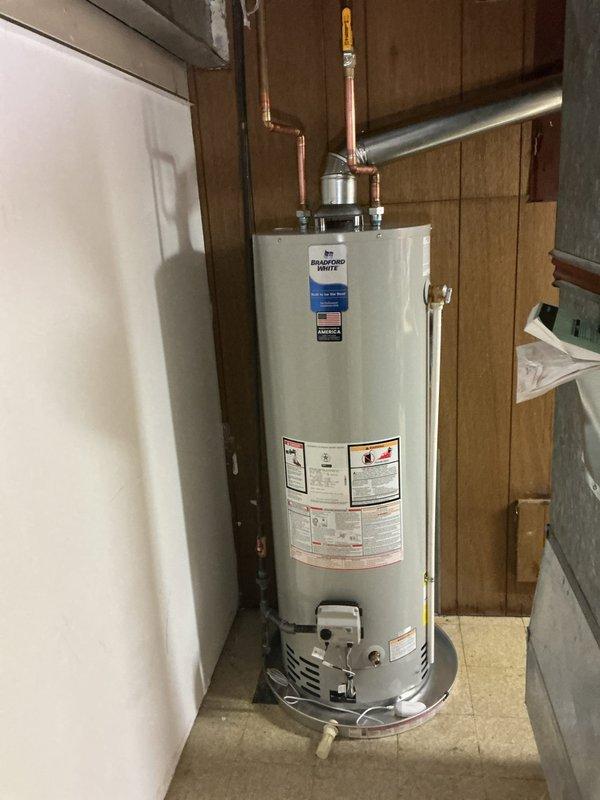 Completed installation of a 40-gallon Bradford White residential water heater in basement utility area. Unit was positioned on level concrete floor between existing wall framing with proper clearances maintained. Connected copper supply and outlet piping with heat trap fittings at top of tank, integrated all connections into existing plumbing system including tie-in at water meter location. Installed chimney liner for proper venting of combustion gases. Verified all manufacturer specifications, safety labels, and operational controls were properly displayed and functional. Tested drain valve operation and confirmed burner assembly installation. System commissioned and operational upon completion.