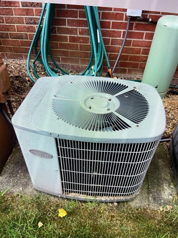 Completed annual preventative maintenance tune-up on 22-year-old Carrier air conditioning system located in basement with outdoor condenser unit. Performed comprehensive inspection including electrical measurements with clamp meter, checked refrigerant levels, cleaned condenser coils, inspected fan operation, verified proper airflow through mesh grille intake, and tested system performance to ensure optimal cooling efficiency for continued operation.