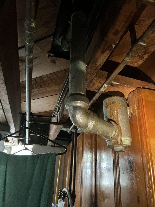Responded to service call for slow draining kitchen sink in downstairs area where water drainage had been progressively worsening over an extended period. Upon arrival, inspected the 50-year-old home's plumbing system and accessed basement infrastructure to evaluate drainage lines and connections. Assessed aged copper and galvanized piping showing oxidation and patina consistent with the home's age. Cleared obstruction from kitchen sink drain line to restore proper water flow. Additionally performed requested maintenance flush of water heater unit located in basement to remove sediment buildup and maintain system efficiency. Inspected exposed plumbing assembly including aged pipe fittings, valve connections, and drainage system. Documented existing plumbing conditions with photographic evidence showing basement infrastructure, wooden floor joists, and aged metallic pipe assemblies with visible oxidation on fittings. Verified no additional drainage issues were present elsewhere in the h