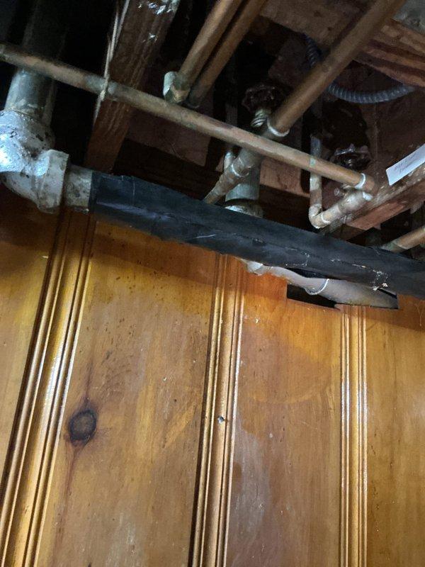 Responded to service call for slow draining kitchen sink in downstairs area where water drainage had been progressively worsening over an extended period. Upon arrival, inspected the 50-year-old home's plumbing system and accessed basement infrastructure to evaluate drainage lines and connections. Assessed aged copper and galvanized piping showing oxidation and patina consistent with the home's age. Cleared obstruction from kitchen sink drain line to restore proper water flow. Additionally performed requested maintenance flush of water heater unit located in basement to remove sediment buildup and maintain system efficiency. Inspected exposed plumbing assembly including aged pipe fittings, valve connections, and drainage system. Documented existing plumbing conditions with photographic evidence showing basement infrastructure, wooden floor joists, and aged metallic pipe assemblies with visible oxidation on fittings. Verified no additional drainage issues were present elsewhere in the h