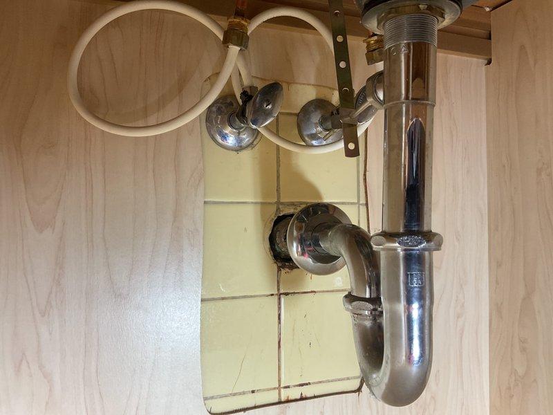 Responded to service call for kitchen and bathroom sink faucets experiencing drainage issues and failure to fully shut off. Inspected kitchen sink plumbing assembly including P-trap, tailpiece, drain assembly with chrome strainer basket, and supply line connections with angle stop valves. Examined bathroom sink installation featuring white oval basin with chrome single-handle faucet and clear acrylic knob handle. Addressed drainage problems in both fixtures and repaired shut-off mechanisms to restore proper water flow control and ensure complete closure of both faucets.
