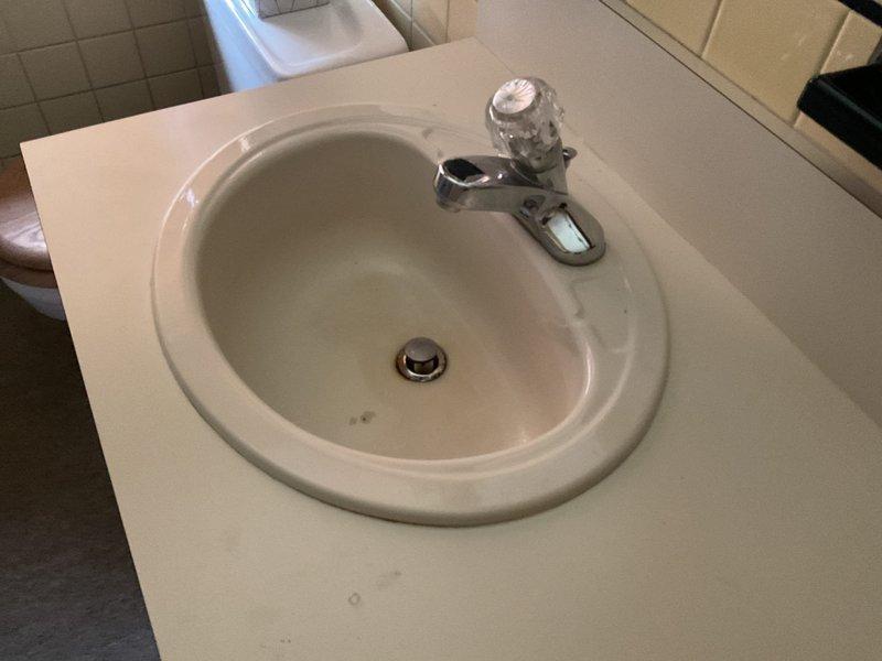 Responded to service call for kitchen and bathroom sink faucets experiencing drainage issues and failure to fully shut off. Inspected kitchen sink plumbing assembly including P-trap, tailpiece, drain assembly with chrome strainer basket, and supply line connections with angle stop valves. Examined bathroom sink installation featuring white oval basin with chrome single-handle faucet and clear acrylic knob handle. Addressed drainage problems in both fixtures and repaired shut-off mechanisms to restore proper water flow control and ensure complete closure of both faucets.