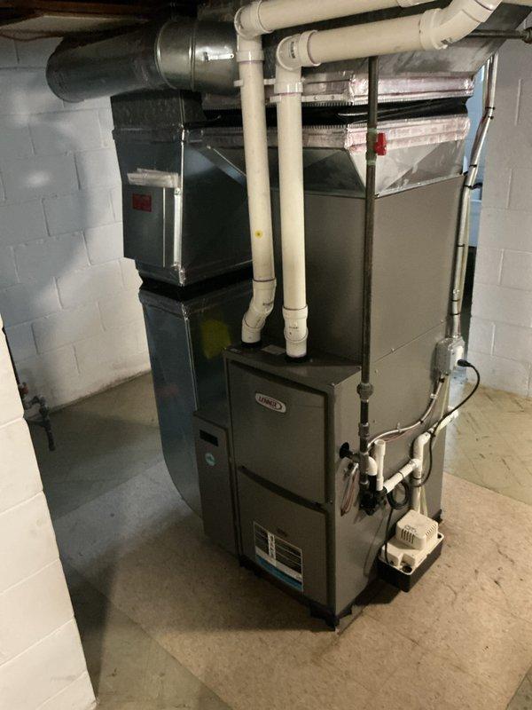 Completed Gold AC Inspection on a 3-year-old residential HVAC system with air handler and furnace located in basement. Verified system operational status, inspected air handler unit with connected ductwork, examined PVC condensate drainage lines, checked furnace components and auxiliary condensate pump with associated piping connections, and confirmed thermostat functionality showing proper temperature control in heating mode at 79°F.