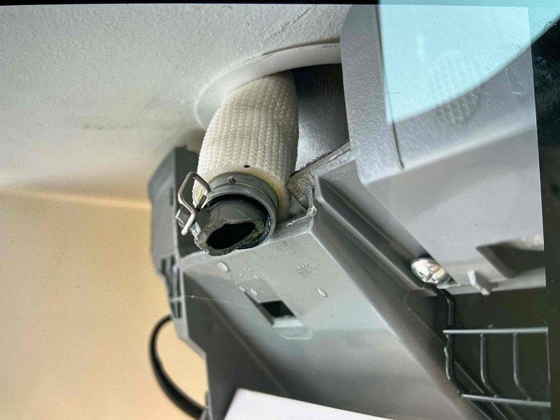 Responded to service call for leaking Mister Cool ductless mini-split system located upstairs. Unit was approximately two years old and still providing adequate cooling despite active water leak. Upon inspection, examined indoor air handler unit, refrigerant line connections, and condensate drainage system. Photographed installation showing flexible ductwork connection, refrigerant lines with insulation, and wall-mounted indoor unit configuration. Assessed condensate drain routing and potential blockage points that could cause water overflow from drain pan. Unit showed normal operational signs with no immediate mechanical failures evident during visual inspection.