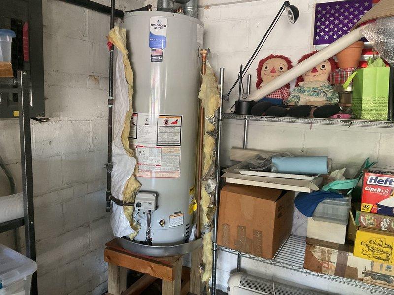 Responded to service call regarding missing insulation wrap on previously installed water heater. Upon inspection, confirmed that original insulation material from prior tank installation had been reused and properly applied to current water heater unit. Verified reflective foil insulation jacket with securing straps was intact and correctly positioned around cylindrical tank body. Documented installation with photographs showing insulation wrap in place, along with yellow foam pipe insulation on connected water lines and proper venting configuration.