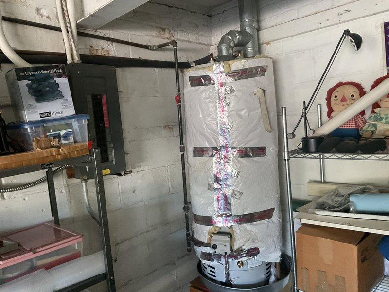 Responded to service call regarding missing insulation wrap on previously installed water heater. Upon inspection, confirmed that original insulation material from prior tank installation had been reused and properly applied to current water heater unit. Verified reflective foil insulation jacket with securing straps was intact and correctly positioned around cylindrical tank body. Documented installation with photographs showing insulation wrap in place, along with yellow foam pipe insulation on connected water lines and proper venting configuration.
