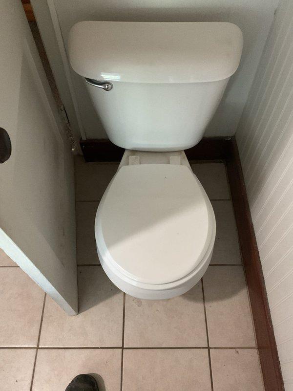 Completed toilet replacement and associated plumbing repair in residential bathroom. Removed existing toilet fixture and addressed drainage system issues requiring access through ceiling from floor above. Installed new white porcelain two-piece toilet with chrome flush handle in narrow bathroom alcove with tile flooring and wood trim. Repaired PVC drainage piping running through ceiling joists, including angled pipe runs and curved joints to ensure proper drainage flow. Patched and prepared ceiling opening for drywall restoration following plumbing repairs. All fixtures tested and verified operational upon completion.