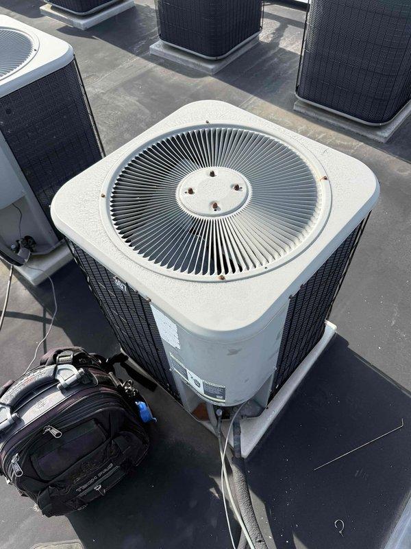 Responded to service call for 20-year-old rooftop A/C unit running but not cooling adequately. Accessed rooftop equipment via internal ladder and performed diagnostic evaluation of the affected condenser unit. Upon inspection, identified and addressed cooling performance issues on the unit with the white and beige housing featuring circular fan grille. Verified proper operation of condenser fan motor, checked refrigerant lines for restrictions, and assessed overall system performance. Restored unit to proper cooling operation and confirmed adequate airflow throughout the system.