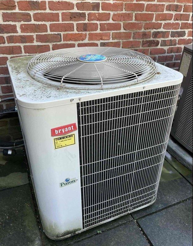 Completed comprehensive Gold AC Inspection on multi-unit residential HVAC system consisting of two outdoor condensing units: one Lennox unit and one Bryant unit, both positioned on exterior concrete pads against brick wall. Performed thorough visual inspection of both condenser units, evaluated physical condition of cabinets showing normal outdoor weathering, verified proper installation on concrete pads, inspected fan guards and louvers for adequate airflow, checked refrigerant labels (Puron), and documented equipment specifications. Noted minor organic growth accumulation around unit bases and dirt buildup consistent with outdoor exposure, though both units remain operational. Equipment located at basement and side of house positions, with upstairs unit being newer installation. All components inspected and photographed for maintenance records.