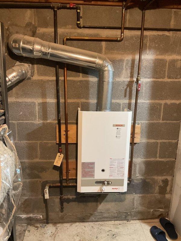 Performed comprehensive tankless water heater flush on Bosch unit located in basement mechanical room. Customer reported decreased water temperature output from the system. Upon inspection, found mineral scale buildup consistent with the home's age and typical hard water conditions in the area affecting heat exchanger efficiency.

Isolated the unit by shutting off gas and water supply valves. Connected descaling pump and circulation hoses to the service valves on both hot and cold water lines. Circulated food-grade descaling solution through the heat exchanger for approximately 45 minutes to dissolve calcium and mineral deposits. Flushed system thoroughly with clean water to remove all descaling solution and loosened sediment. Inspected inline water filter screen and cleaned debris. Tested all gas connections for leaks using soap solution. Verified proper venting integrity on the exhaust system extending through the cinder block wall. Restored water and gas supply, then fired unit to v