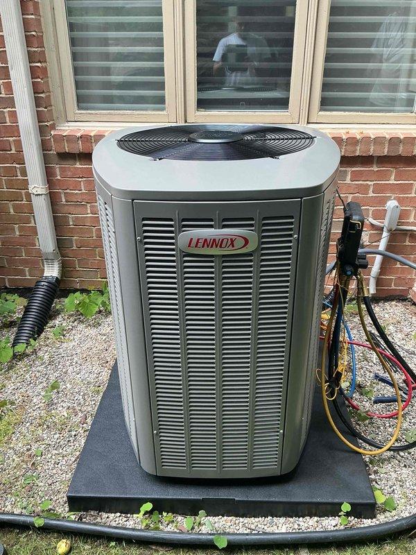 Completed installation of 5-ton Lennox air conditioning system with matching evaporator coil at rear of residence. Installed outdoor condenser unit on rubber pad with gravel base, positioned adjacent to brick exterior wall with proper clearances. Connected refrigerant lines with service ports, completed electrical connections, and installed white PVC condensate drainage. Indoor air handler installed in utility room with beige tile flooring, equipped with condensate pump for proper drainage management. Performed system flush and refrigerant line connections. All mechanical work completed per permit requirements with reconnection of existing electrical components.