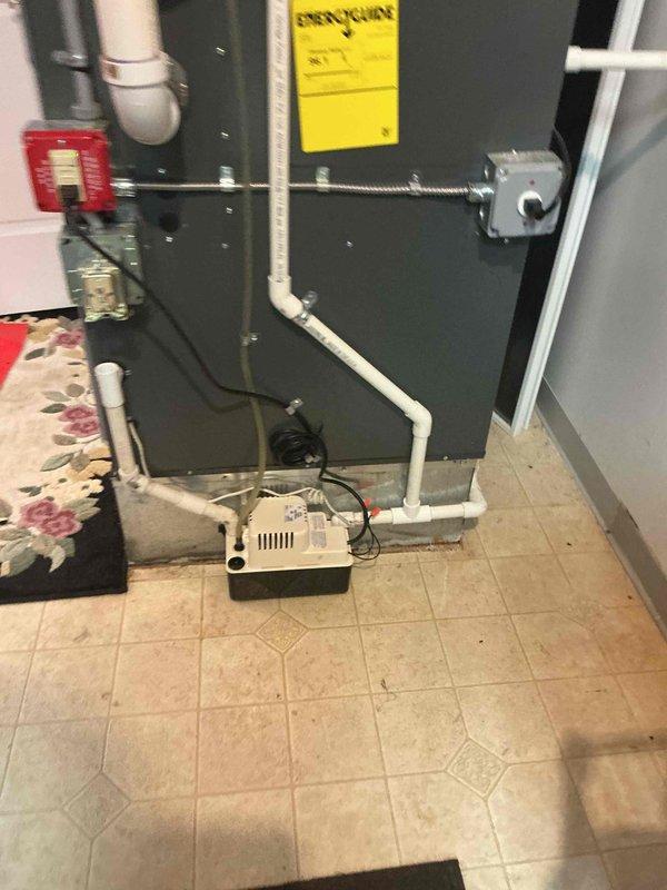 Completed installation of 5-ton Lennox air conditioning system with matching evaporator coil at rear of residence. Installed outdoor condenser unit on rubber pad with gravel base, positioned adjacent to brick exterior wall with proper clearances. Connected refrigerant lines with service ports, completed electrical connections, and installed white PVC condensate drainage. Indoor air handler installed in utility room with beige tile flooring, equipped with condensate pump for proper drainage management. Performed system flush and refrigerant line connections. All mechanical work completed per permit requirements with reconnection of existing electrical components.