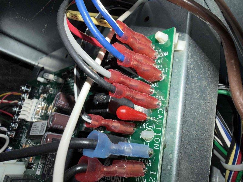 Responded to service call for loud noises coming from 2022 AC condenser unit located in basement. Upon arrival, performed diagnostic testing using refrigerant leak detector and inspected control board wiring connections. Examined thermostat wiring configuration at control panel, checking COM, SAT, HEAT, and COOL terminal connections for proper seating and signs of arcing or deterioration. Verified all wire terminations were secure and heat-shrink connections were intact. Completed system evaluation and documented findings with photographs for service records.