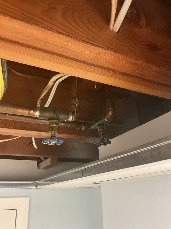 Responded to basement water leak originating from deteriorated shutoff valve in 60-year-old residential plumbing system. Upon inspection, identified corroded copper piping with significant green patina and aging brass fittings in exposed ceiling joists. Replaced faulty shutoff valve with blue-handled ball valve, secured all connections, and tested system under pressure to confirm leak elimination. Documented existing plumbing infrastructure condition with photographic evidence showing oxidized copper lines and vintage fittings typical of original installation.