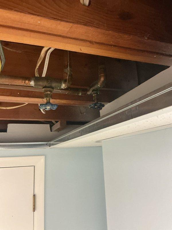 Responded to basement water leak originating from deteriorated shutoff valve in 60-year-old residential plumbing system. Upon inspection, identified corroded copper piping with significant green patina and aging brass fittings in exposed ceiling joists. Replaced faulty shutoff valve with blue-handled ball valve, secured all connections, and tested system under pressure to confirm leak elimination. Documented existing plumbing infrastructure condition with photographic evidence showing oxidized copper lines and vintage fittings typical of original installation.