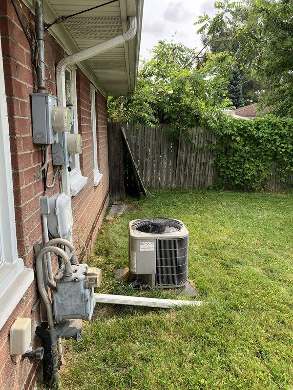 Conducted site assessment for HVAC equipment replacement estimate at residential property with natural gas heating system. Evaluated existing outdoor air conditioning unit located on concrete pad in side yard, along with associated electrical components, meters, and gas service connections mounted on exterior brick wall. Documented current equipment configuration and utility infrastructure to provide comprehensive replacement recommendations.