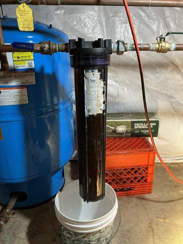 Responded to low water pressure complaint affecting entire residence. Upon inspection of water filtration system in crawl space, confirmed water filter cartridge was cross-threaded in housing, restricting flow throughout plumbing system. Removed improperly installed filter cartridge from transparent housing unit connected to main water line and blue pressure tank assembly. Cleaned housing threads to ensure proper sealing, installed new filter cartridge with correct threading and torque specifications, and verified all connections were secure. Tested system operation and confirmed full water pressure restoration to all fixtures throughout home.