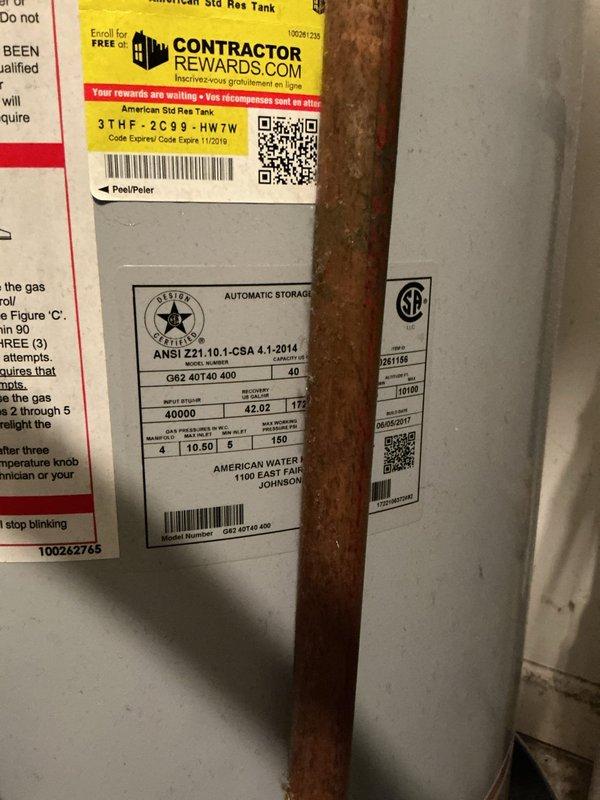 Responded to emergency water leak at residential property where 40-gallon American Standard atmospheric vent gas water heater was actively leaking, causing water damage to the unit and condo below. Upon arrival, water supply had already been shut off at the tank by occupant. Conducted thorough inspection of the unit located in upstairs laundry room and documented extensive corrosion at pipe connections and fittings on top of tank, particularly around the cold water inlet with blue dielectric union showing severe rust deposits and deterioration. Observed significant oxidation on copper supply lines and corroded pipe joints throughout the plumbing assembly. Tank specifications confirmed as 40-gallon capacity, 40,000 BTU input, manufactured by American Water Heater Company. Photographed corroded connections, rusted fittings, and compromised plumbing assembly showing advanced age-related deterioration as source of leak. Advised that water heater has reached end of service life and requires