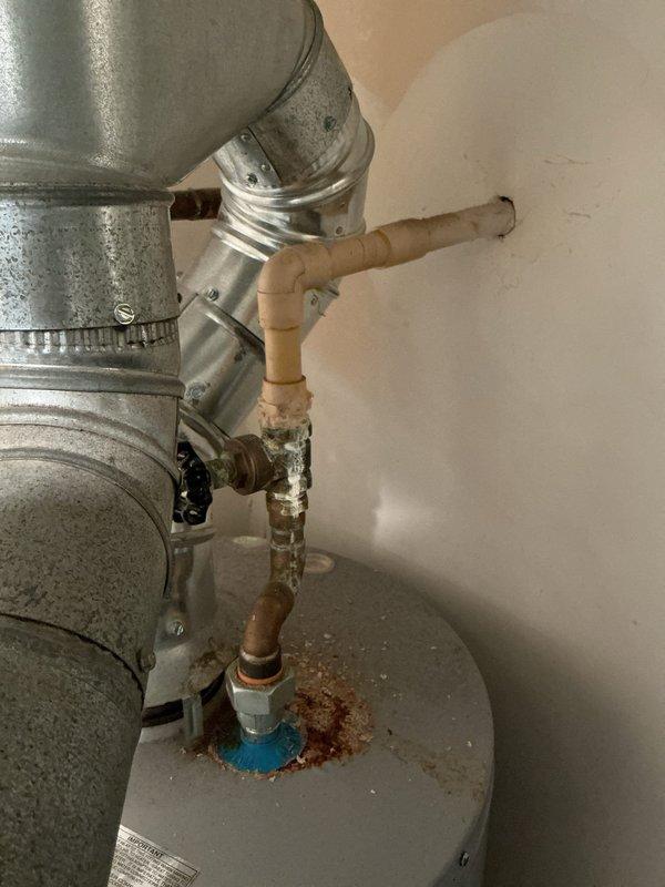 Responded to emergency water leak at residential property where 40-gallon American Standard atmospheric vent gas water heater was actively leaking, causing water damage to the unit and condo below. Upon arrival, water supply had already been shut off at the tank by occupant. Conducted thorough inspection of the unit located in upstairs laundry room and documented extensive corrosion at pipe connections and fittings on top of tank, particularly around the cold water inlet with blue dielectric union showing severe rust deposits and deterioration. Observed significant oxidation on copper supply lines and corroded pipe joints throughout the plumbing assembly. Tank specifications confirmed as 40-gallon capacity, 40,000 BTU input, manufactured by American Water Heater Company. Photographed corroded connections, rusted fittings, and compromised plumbing assembly showing advanced age-related deterioration as source of leak. Advised that water heater has reached end of service life and requires