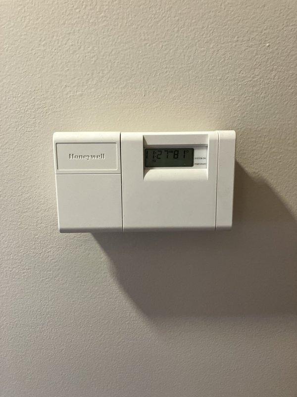 Conducted on-site assessment for cooling system replacement in small residential property (0-1500 sq.ft.) with basement unit location. Evaluated existing Honeywell thermostat and documented current HVAC infrastructure including exposed ductwork, electrical wiring, and utility routing in unfinished basement ceiling area to determine equipment specifications and installation requirements for new cooling system.