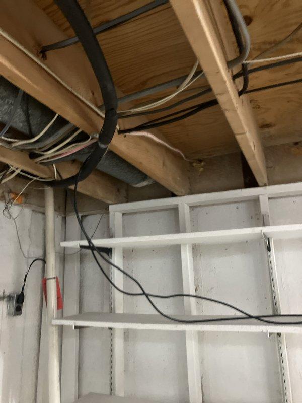 Conducted on-site assessment for cooling system replacement in small residential property (0-1500 sq.ft.) with basement unit location. Evaluated existing Honeywell thermostat and documented current HVAC infrastructure including exposed ductwork, electrical wiring, and utility routing in unfinished basement ceiling area to determine equipment specifications and installation requirements for new cooling system.