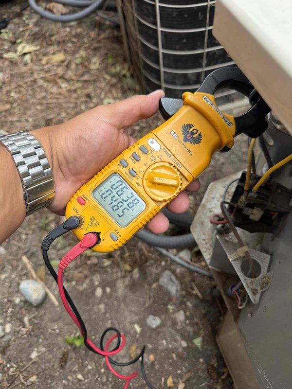 Completed comprehensive Gold AC inspection on 10+ year old residential air conditioning system with air handler located in basement. Performed electrical diagnostics using clamp meter to verify proper amperage draw and system performance. Inspected outdoor condenser unit and noted debris accumulation at base including organic material and vegetation growth, as well as dust buildup in condenser coil fins. Confirmed system is currently operational. Documented equipment condition through photography for maintenance records. Homeowner present during inspection of single-unit system.