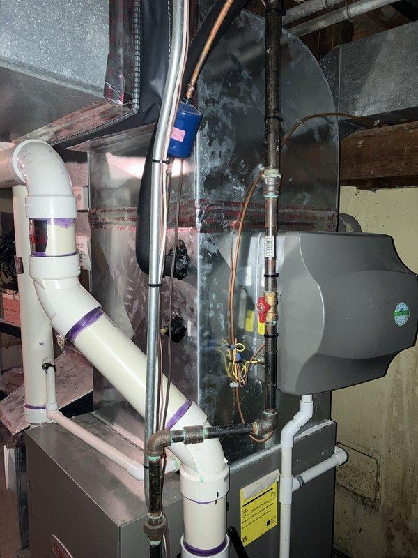 Performed comprehensive leak test on 15-year-old residential air conditioning system located in basement following previous refrigerant recharge requirement. Inspected Lennox air handler unit, refrigerant lines, brass valve assembly, and associated copper tubing for potential leak points. Evaluated system components including condensate drainage configuration with PVC piping, electrical connections, and refrigerant line insulation integrity to identify source of refrigerant loss and determine viability of repair versus replacement recommendation.