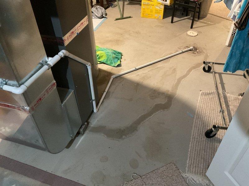 Responded to water leak call in basement near furnace in 26-year-old home. Upon inspection, identified clogged condensate drain line on HVAC air handler unit as source of water damage to basement floor. Cleared blockage from condensate line using appropriate tools and verified proper drainage flow through PVC piping system. Tested air handler operation to ensure condensate was draining correctly through cleared line. Documented existing water staining on subflooring from previous leak occurrence. System restored to normal operation with condensate draining freely.