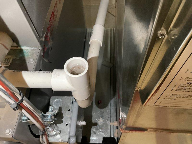 Responded to water leak call in basement near furnace in 26-year-old home. Upon inspection, identified clogged condensate drain line on HVAC air handler unit as source of water damage to basement floor. Cleared blockage from condensate line using appropriate tools and verified proper drainage flow through PVC piping system. Tested air handler operation to ensure condensate was draining correctly through cleared line. Documented existing water staining on subflooring from previous leak occurrence. System restored to normal operation with condensate draining freely.