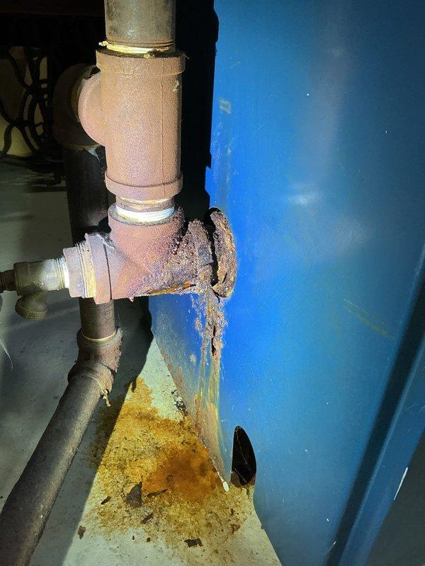 Responded to water leak investigation related to boiler piping system. Upon arrival, performed diagnostic assessment of heating system and associated plumbing connections near blue pressure tank. Identified active leak originating from boiler piping assembly with visible water damage, mineral deposits, and rust staining on concrete floor beneath affected piping. Documented extensive crystalline buildup on horizontal pipe sections and deterioration of tank exterior. Photographed compromised plumbing connections, including insulated elbow joints and vertical pipe assemblies showing signs of moisture intrusion. Confirmed leak source at boiler piping connections as previously diagnosed by HVAC technician. Customer advised that formal repair estimate will be required to address boiler piping system repairs and resolve ongoing water leak issue.