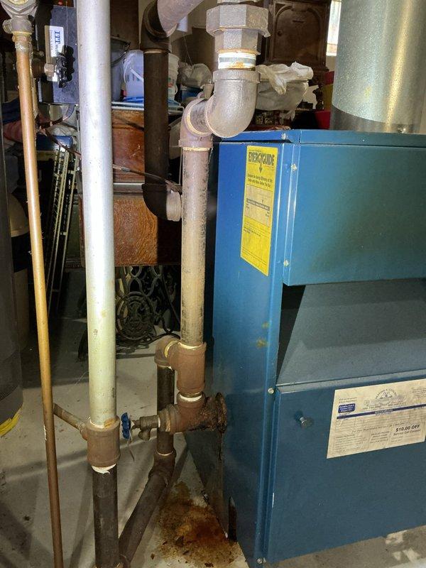 Responded to water leak investigation related to boiler piping system. Upon arrival, performed diagnostic assessment of heating system and associated plumbing connections near blue pressure tank. Identified active leak originating from boiler piping assembly with visible water damage, mineral deposits, and rust staining on concrete floor beneath affected piping. Documented extensive crystalline buildup on horizontal pipe sections and deterioration of tank exterior. Photographed compromised plumbing connections, including insulated elbow joints and vertical pipe assemblies showing signs of moisture intrusion. Confirmed leak source at boiler piping connections as previously diagnosed by HVAC technician. Customer advised that formal repair estimate will be required to address boiler piping system repairs and resolve ongoing water leak issue.