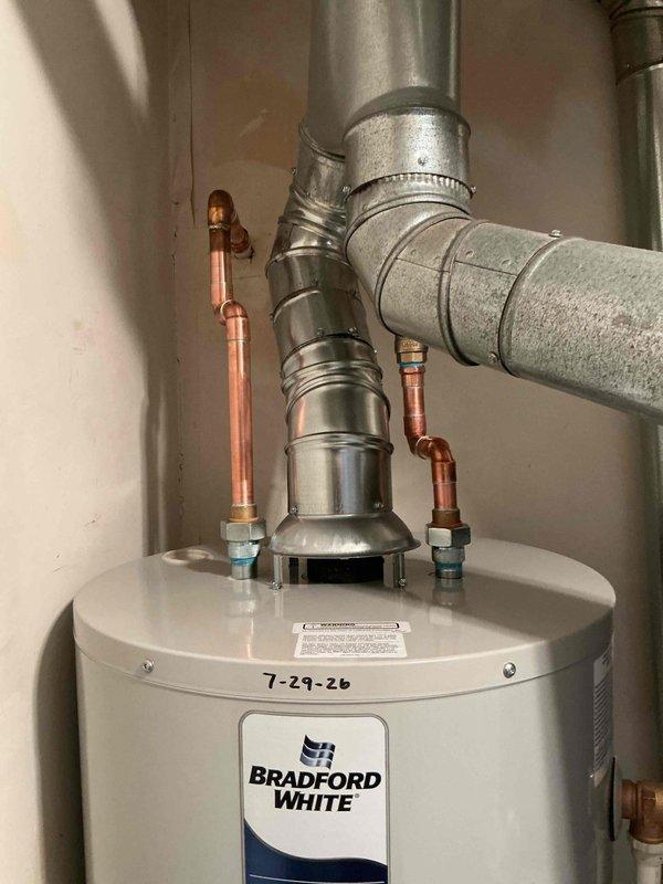 Installed a 40-gallon Bradford White tanked water heater in the utility area. Connected copper supply lines with compression fittings to the inlet and outlet ports, installed proper venting using galvanized ductwork with elbow configuration, and secured all pipes and ducts with metal clamps per manufacturer specifications.